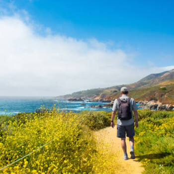 Man hiking alone on vacation. Summer mountain coastal landscape. View from highway 1. Big Sur, California, USA.